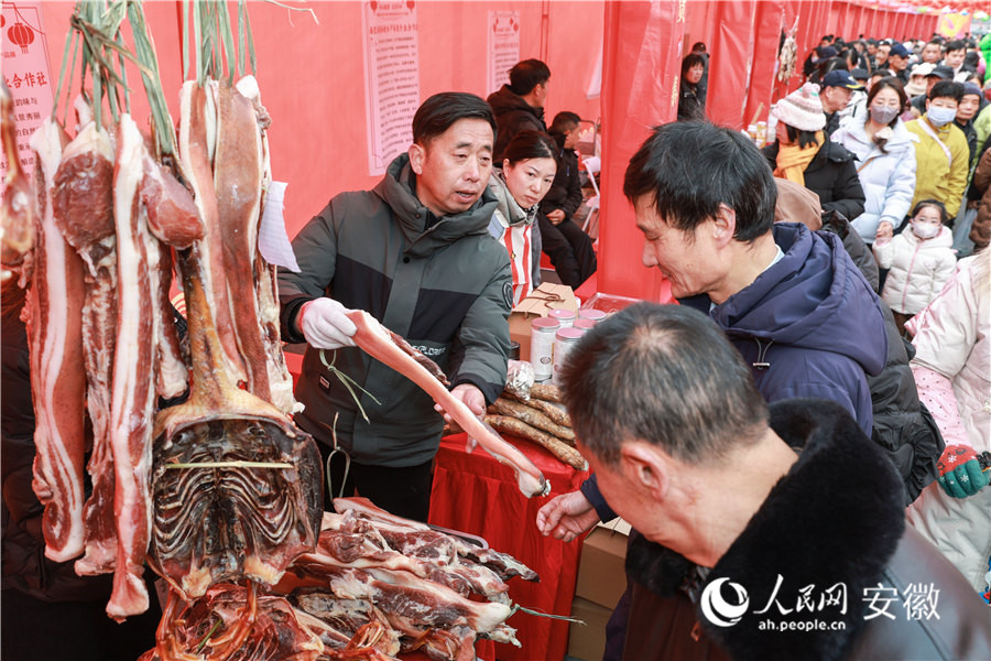南陵年貨集市現(xiàn)場，攤主向顧客推介自家生產(chǎn)的臘肉。人民網(wǎng)記者 張俊攝